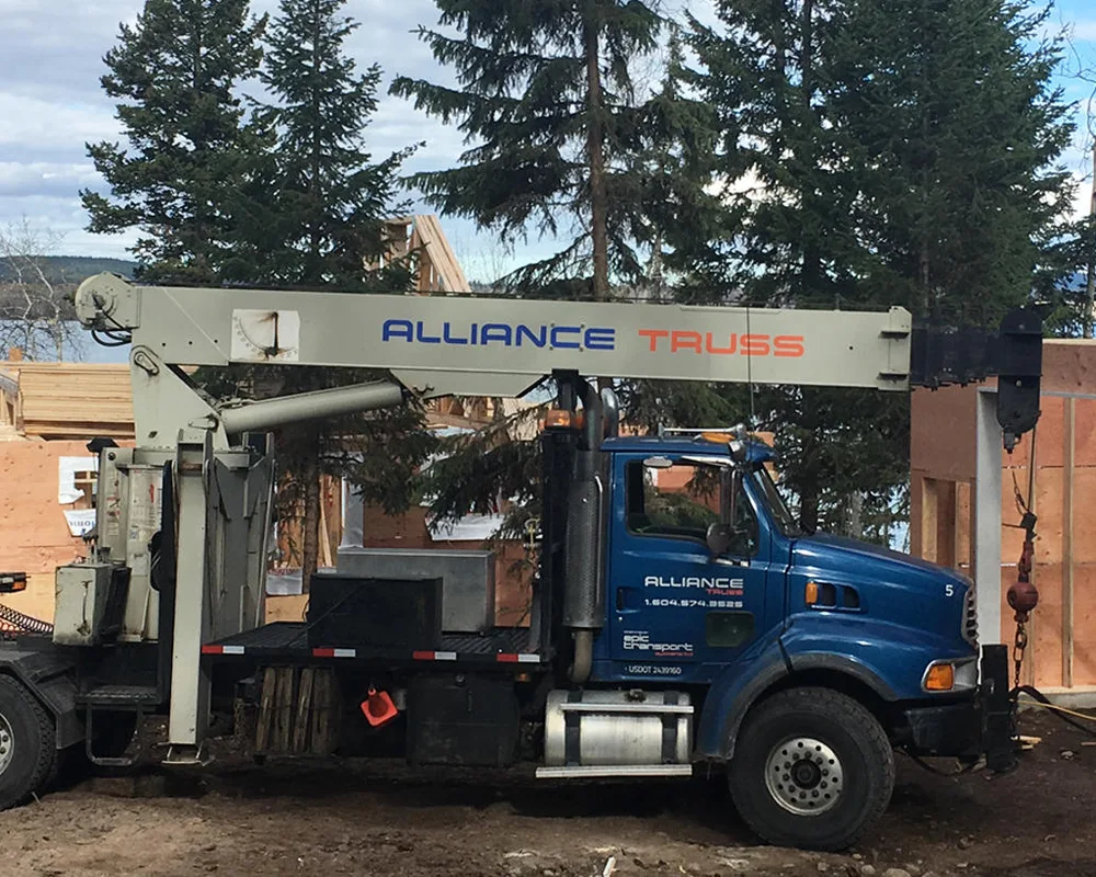 Mobile crane truck with attached trailers parked at a residential work site surrounded by trees.